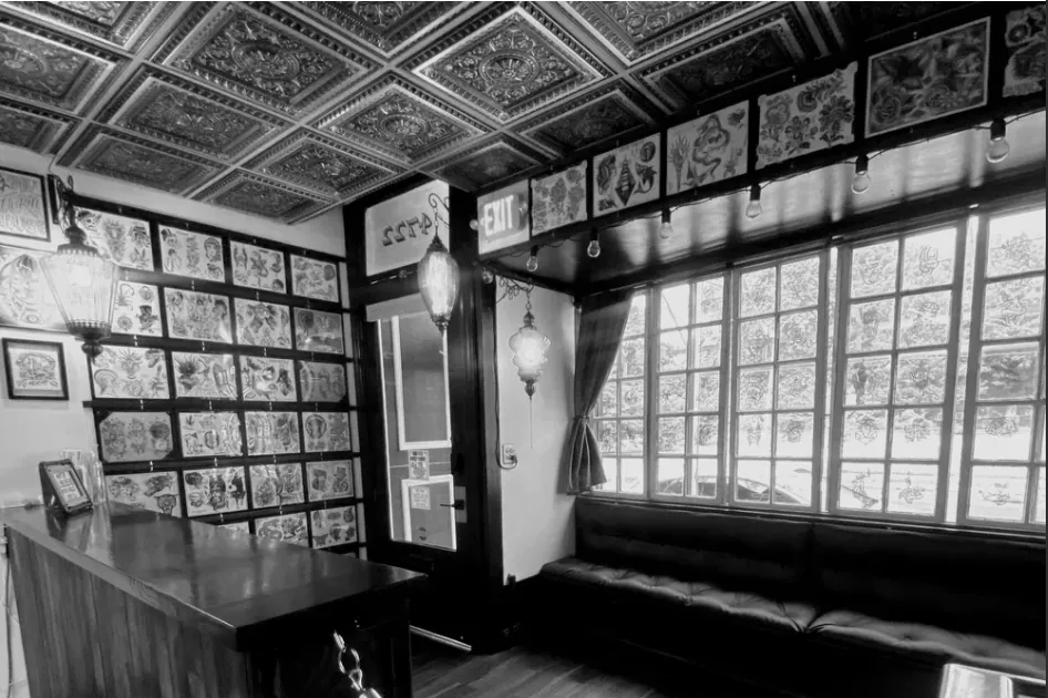 The interior of Sign of the Times Tattoo — pressed-tin ceiling, wall of flash sheets, and a leather bench by the front windows.